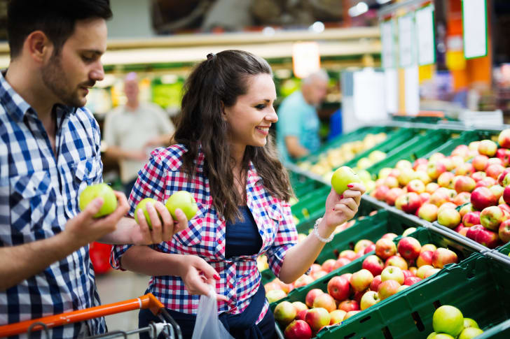 Um homem e uma mulher olhando maçãs no supermercado.