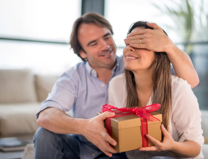 Um homem coloca a mão sobre os olhos de sua parceira enquanto lhe entrega um presente.
